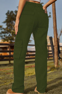 Person wearing green cargo pants in an outdoor setting with a wooden fence and trees.