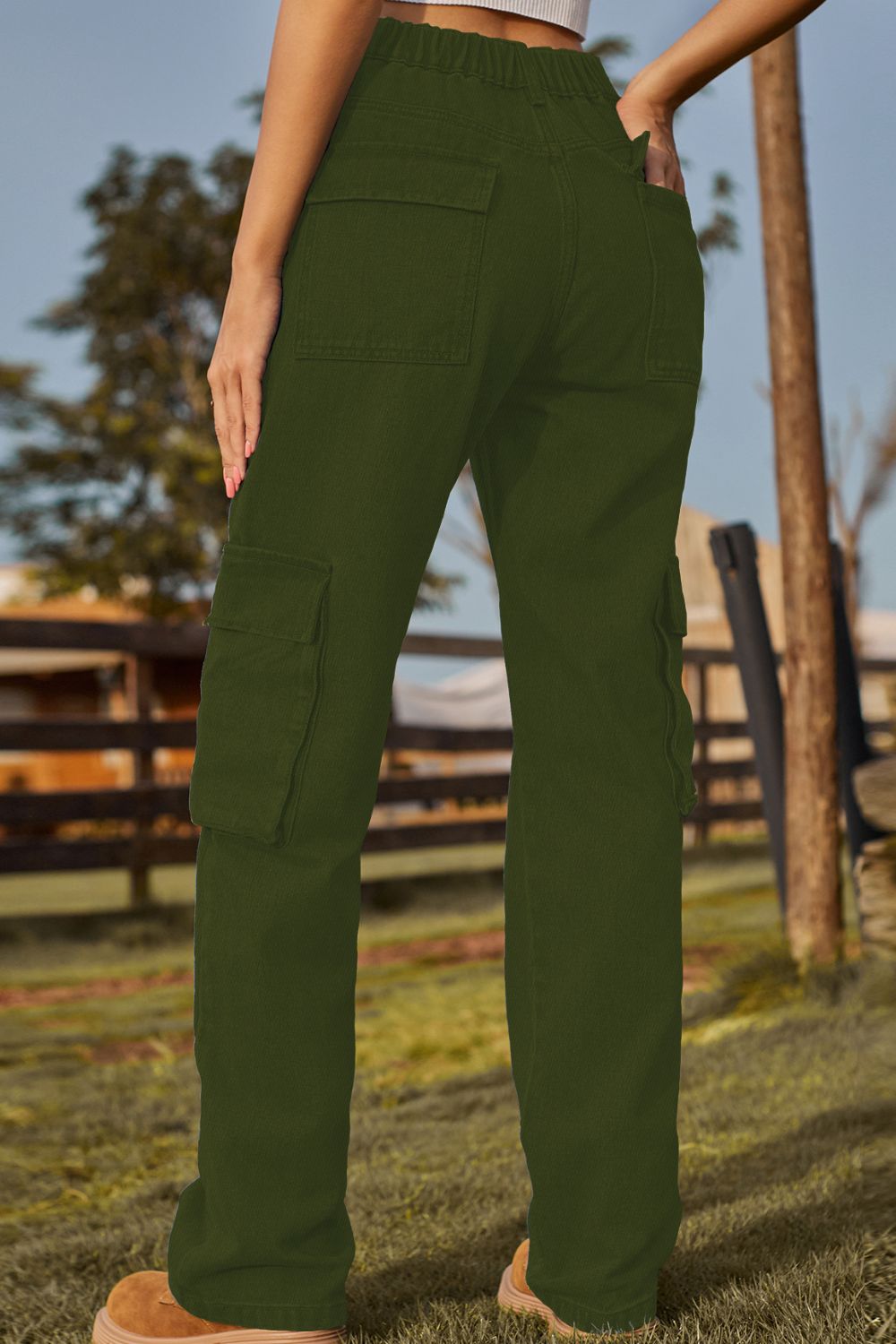 Person wearing green cargo pants in an outdoor setting with a wooden fence and trees.