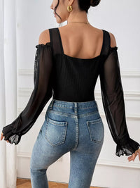 Person wearing a black top with sheer sleeves and blue jeans in a neutral setting