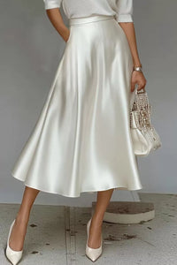 Person wearing a white satin skirt with a plain background