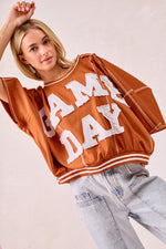 Person wearing a 'GAMEDAY' orange sweatshirt with light blue jeans on a plain background