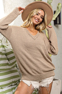 Woman wearing a beige sweater and hat, standing in front of a striped towel and plant.