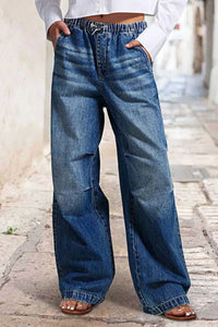 Person wearing wide-leg blue jeans on a blurred street background