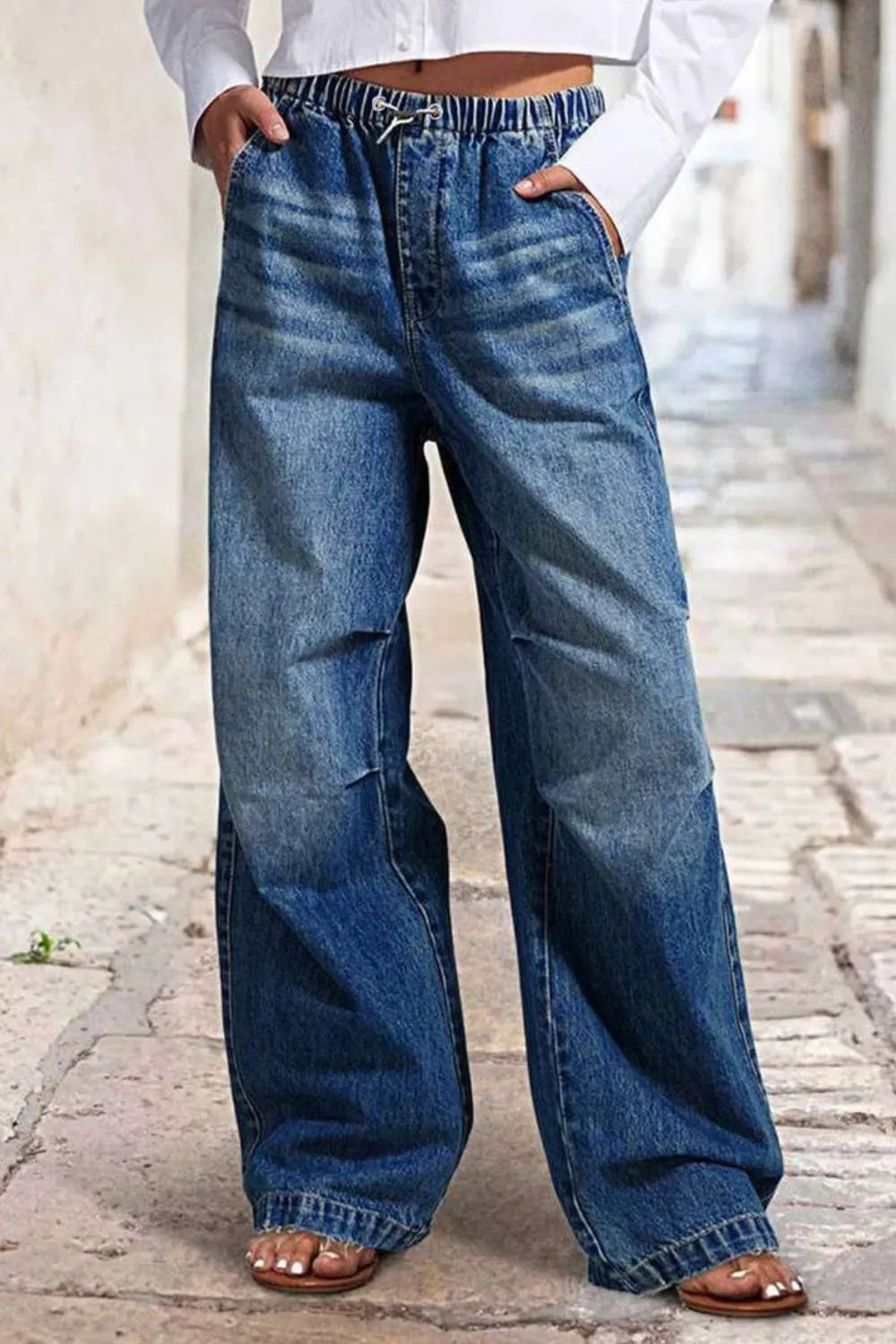Person wearing wide-leg blue jeans on a blurred street background