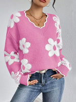 Person wearing a pink sweater with white floral patterns and blue jeans on a gray background