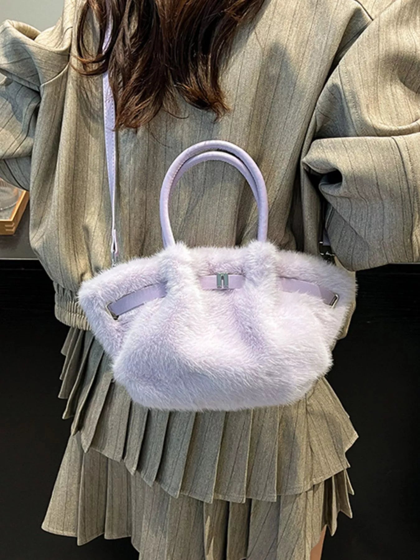 Person wearing a light gray jacket and skirt with a fluffy white handbag.