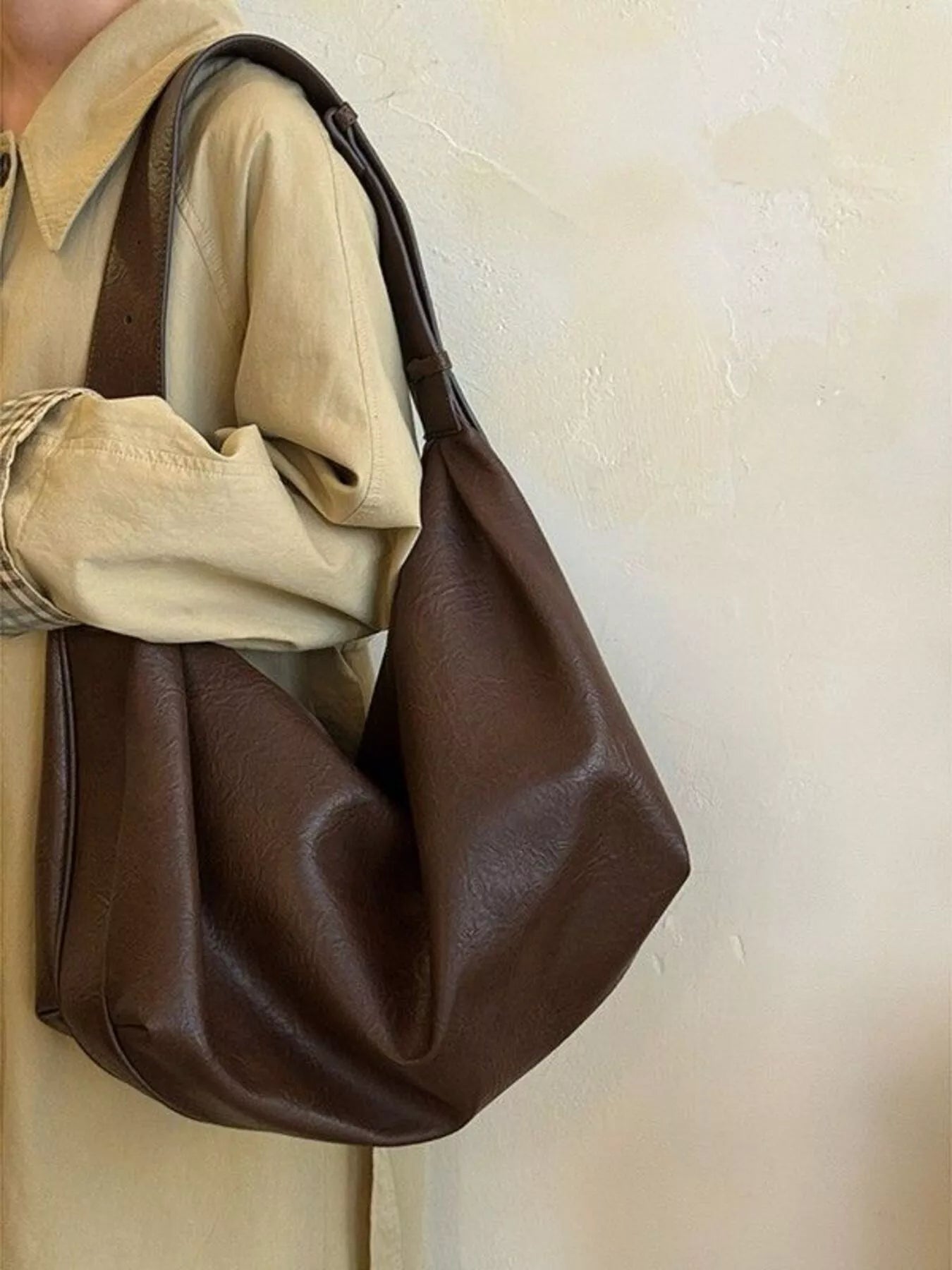 Brown leather handbag held by a person wearing a beige shirt against a plain background