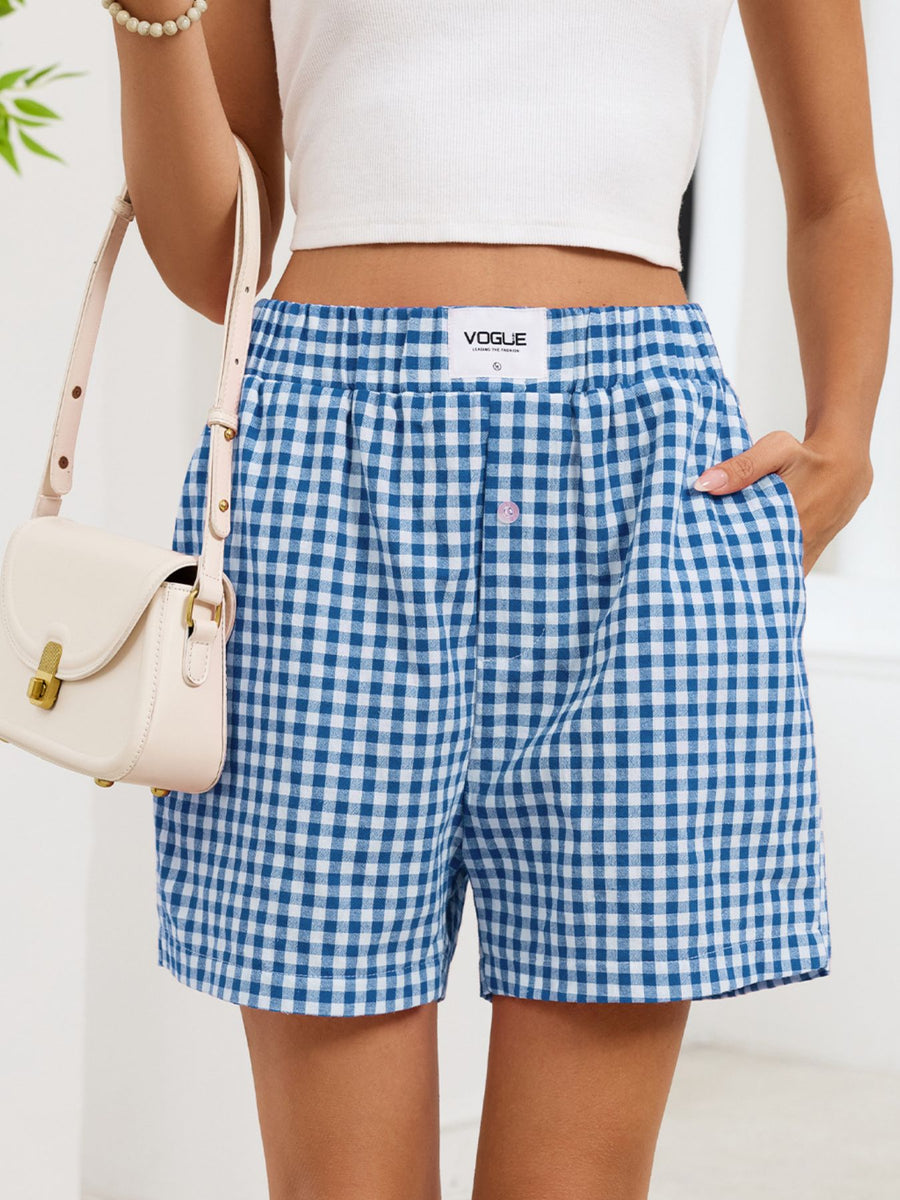Person wearing blue and white checkered shorts with a visible brand logo, holding a beige handbag.