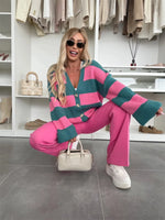 Woman in a pink and green striped cardigan and pink pants posing in a closet.