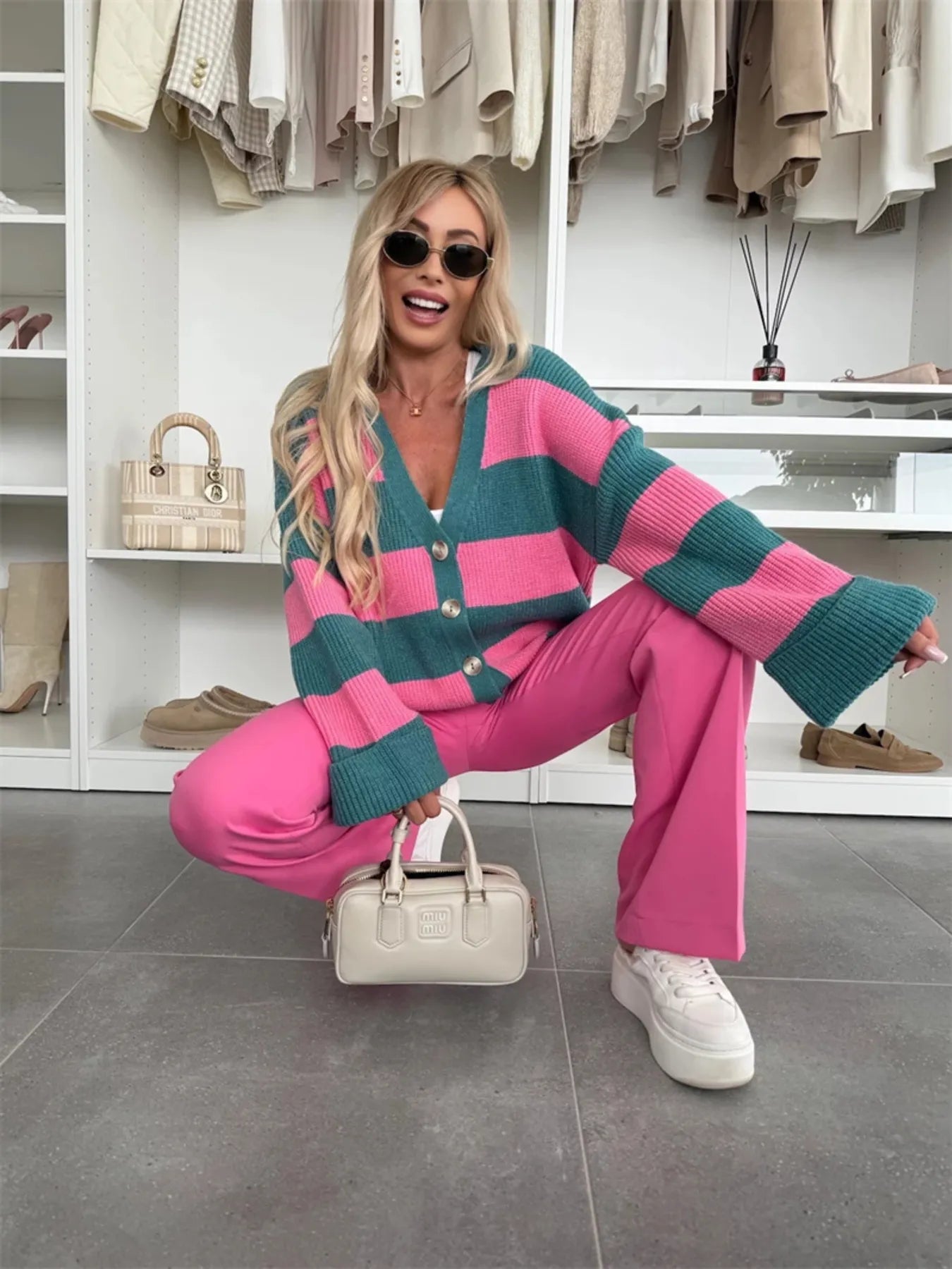 Woman in a pink and green striped cardigan and pink pants posing in a closet.
