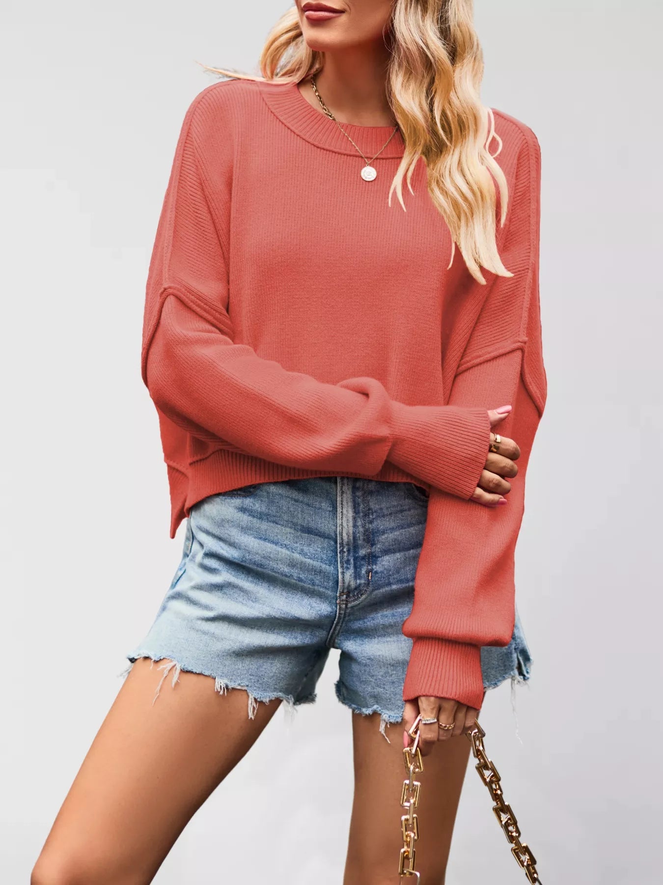 Person wearing a pink sweater and denim shorts on a plain background