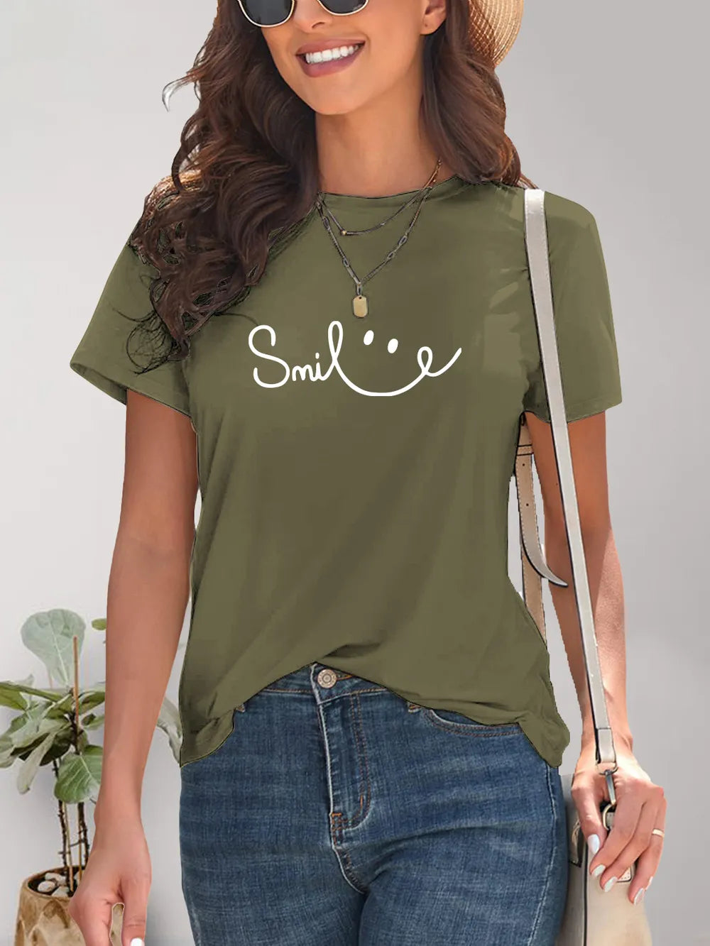 Woman wearing an olive green t-shirt with 'Smile' text, standing against a neutral background.