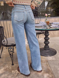 Person wearing light blue jeans standing outdoors near a table with a glass top.