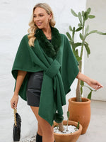 Woman wearing a green poncho with fur trim in an indoor setting.
