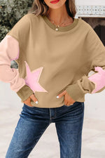 A woman wearing a beige crewneck sweatshirt with light pink star-shaped patches on the front and light pink elbow patches, paired with blue jeans.