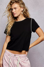 Woman wearing a black crop top and pink pants against a gray background