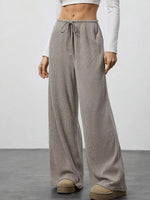 Person wearing beige wide-leg pants with a white top on a plain background
