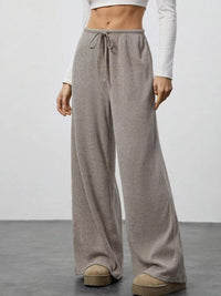 Person wearing beige wide-leg pants with a white top on a plain background