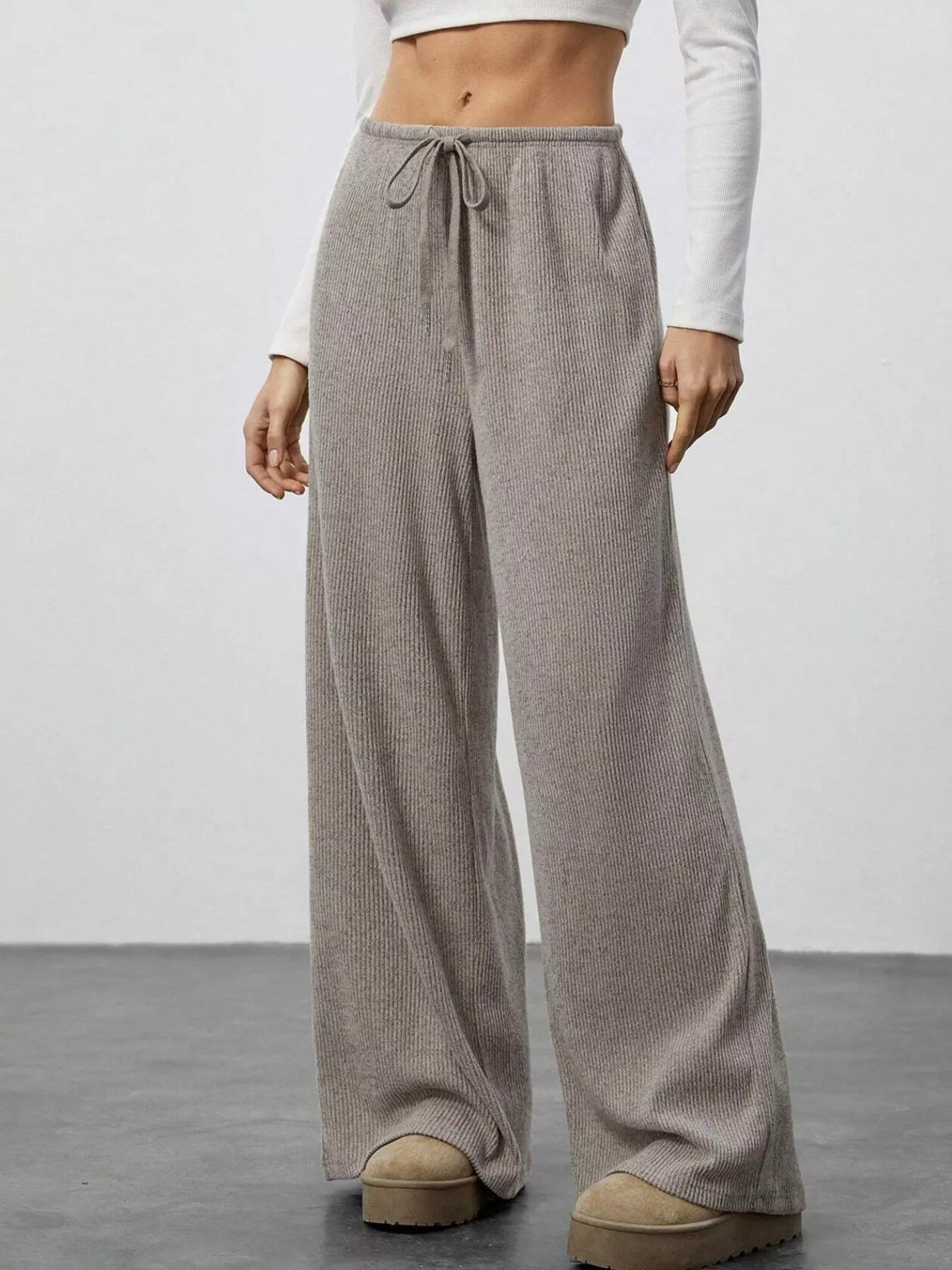 Person wearing beige wide-leg pants with a white top on a plain background