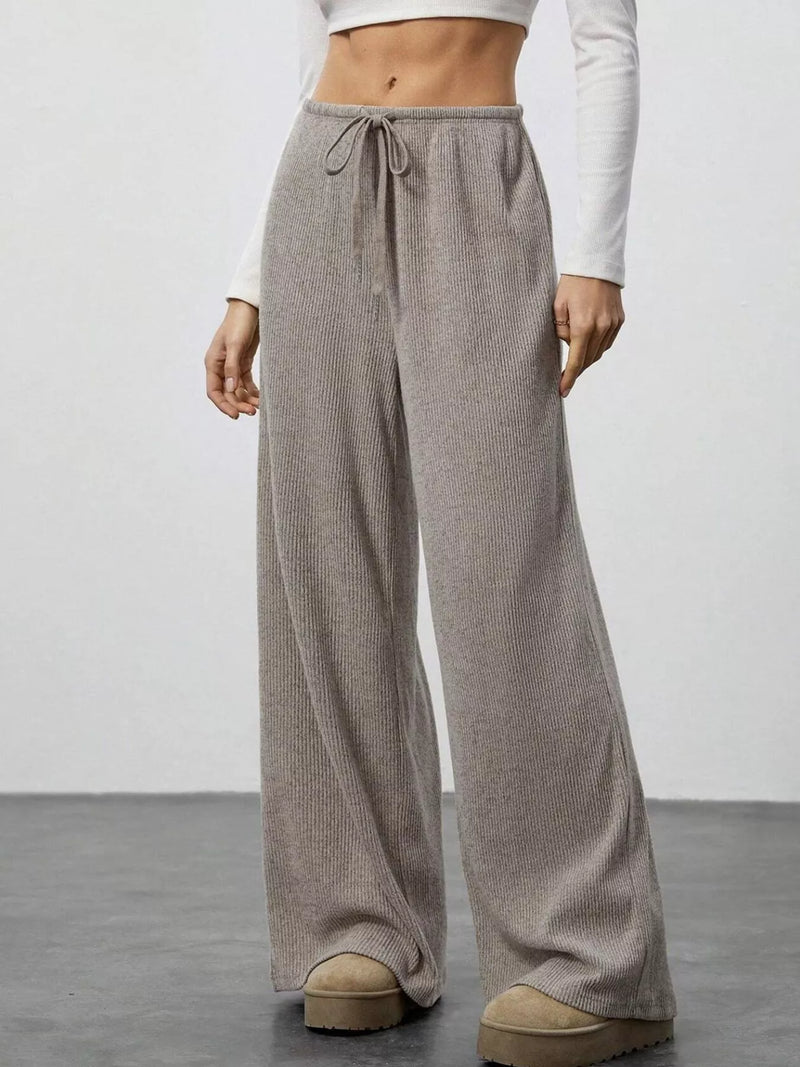 Person wearing beige wide-leg pants with a white top on a plain background
