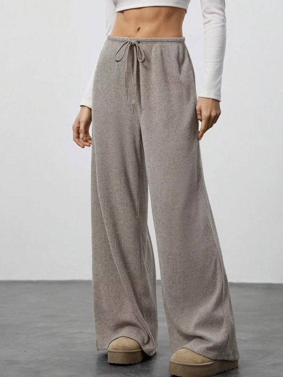 Person wearing beige wide-leg pants with a white top on a plain background