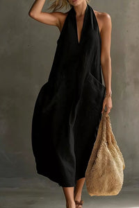 Woman in a black dress holding a beige bag against a gray background