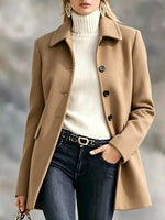 A woman wearing a camel brown tailored coat over a cream ribbed turtleneck sweater, paired with dark blue jeans and a black belt with a gold buckle.