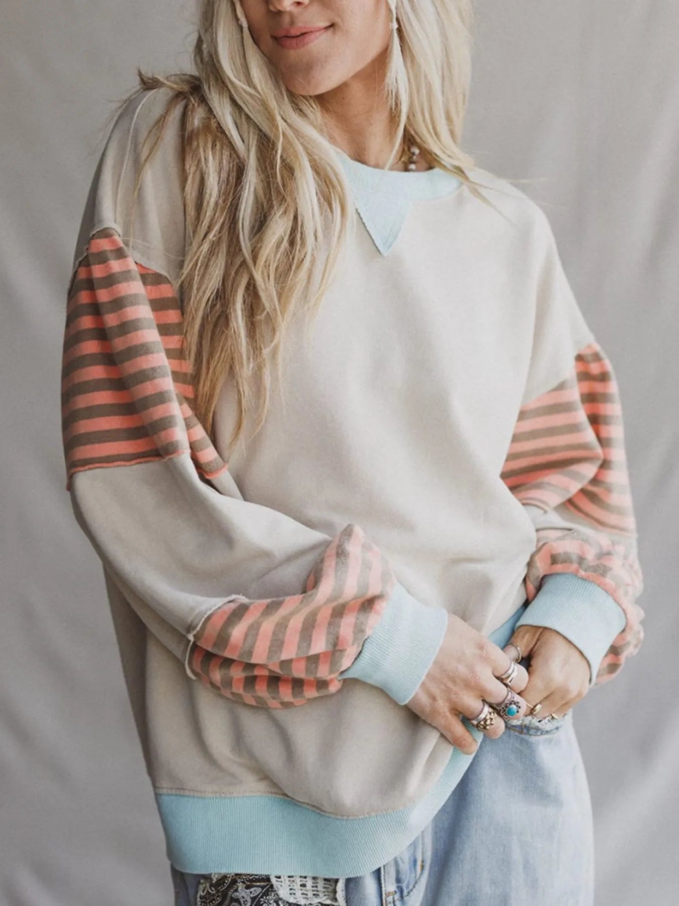 Person wearing a beige sweater with striped sleeves on a plain background