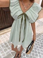 Woman wearing a green and white striped dress with a bow detail on a cobblestone street.