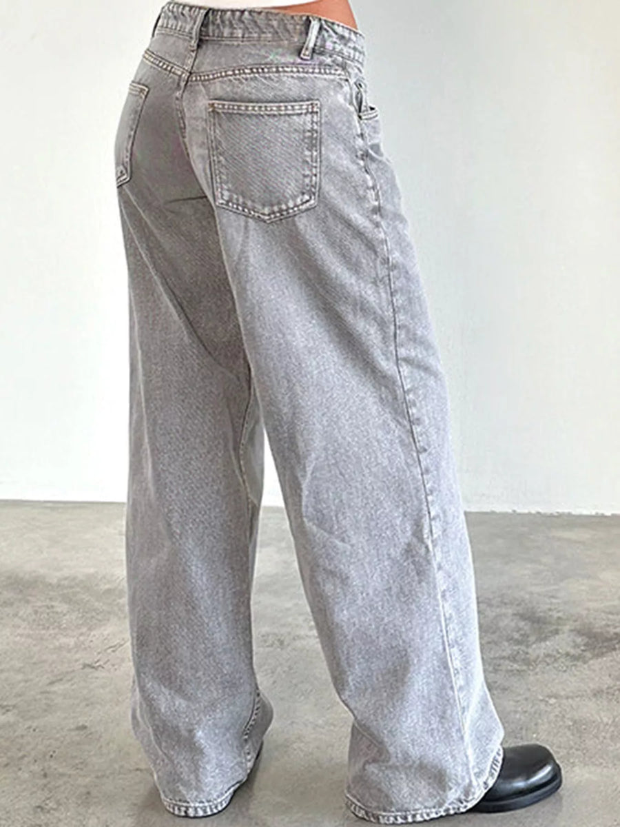 A person wearing light gray wide-leg denim jeans, shown from the back against a plain off-white wall and concrete floor.