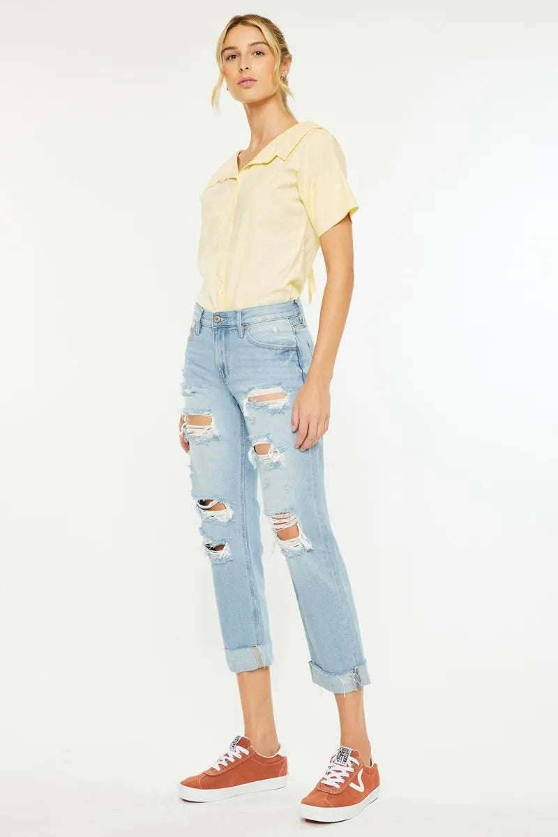Woman wearing a light yellow top and ripped blue jeans on a white background