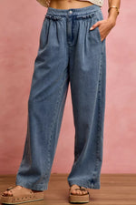 Person wearing blue wide-leg jeans against a pink background