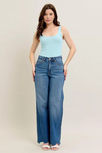 Woman wearing a light blue tank top and high-waisted jeans on a plain background