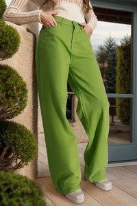 Person wearing bright green pants standing indoors with a blurred outdoor background