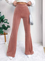 Person wearing pink ribbed pants with a white sweater and silver bag indoors.