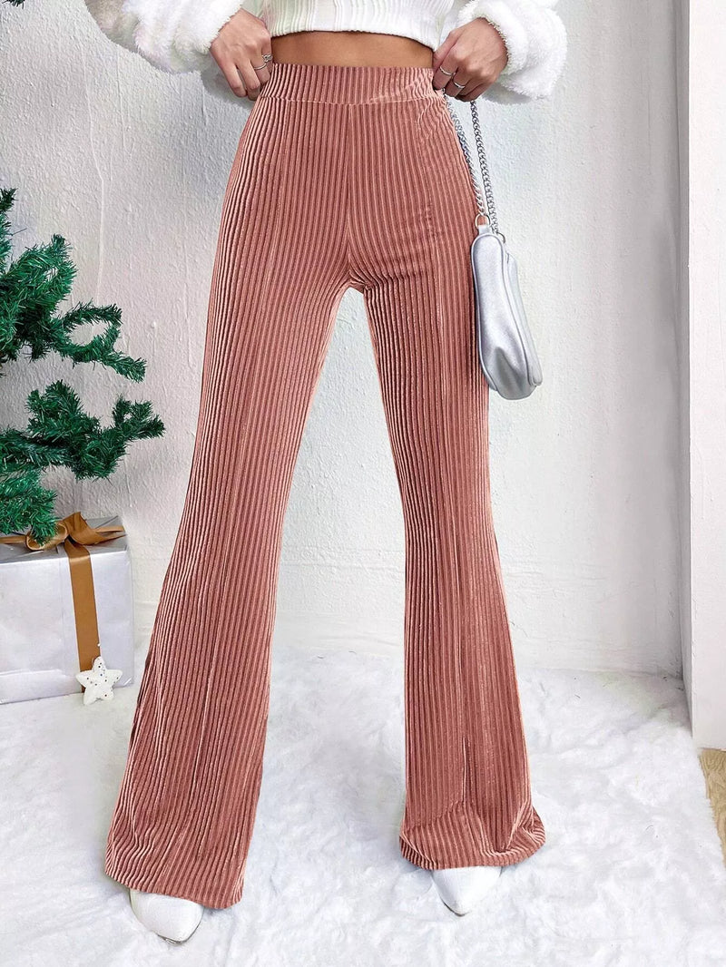 Person wearing pink ribbed pants with a white sweater and silver bag indoors.