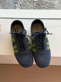 Pair of dark blue sneakers with green stripes on a wooden surface.