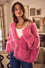 Woman wearing a pink fuzzy cardigan in a cozy living room.