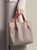 Person holding a gray handbag with brown handles and trim.