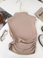 Beige sleeveless top on a hanger with a magazine and books in the background