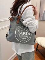 Person holding a gray tote bag with 'Paris' text in a room.