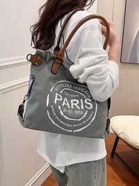 Person holding a gray tote bag with 'Paris' text in a room.