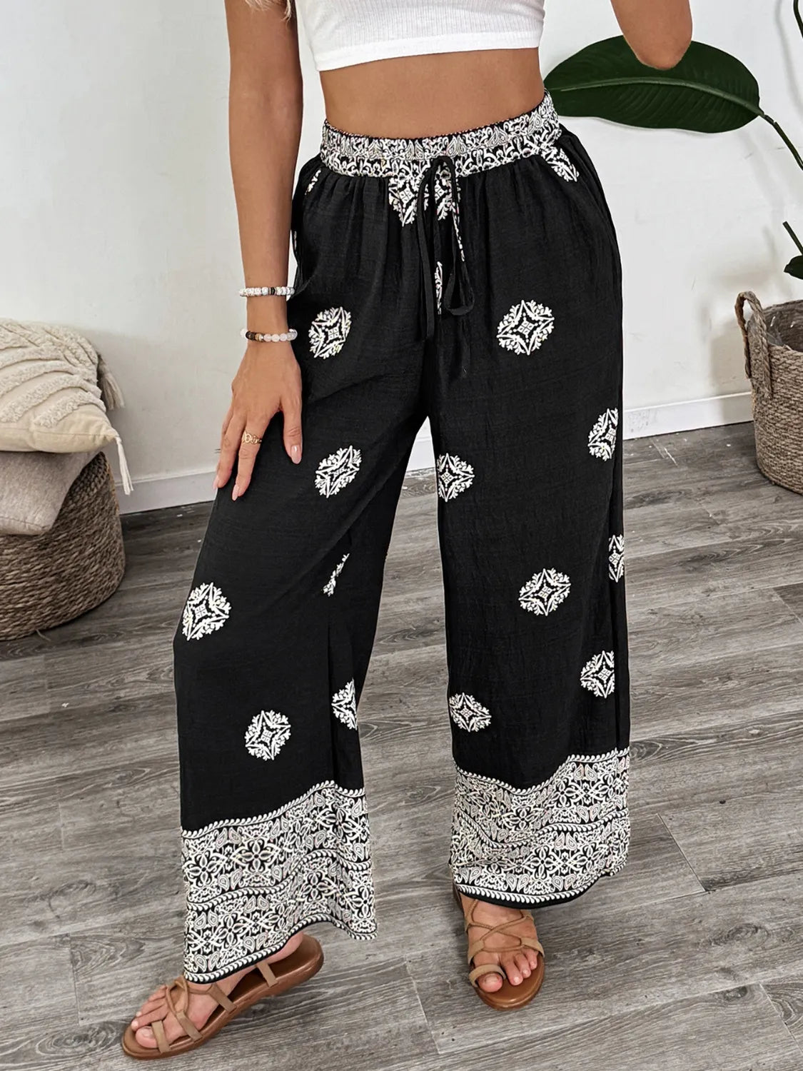 Person wearing black wide-leg pants with white floral patterns indoors.