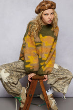 Person wearing a patterned sweater and beret sitting on a stool against a gray background