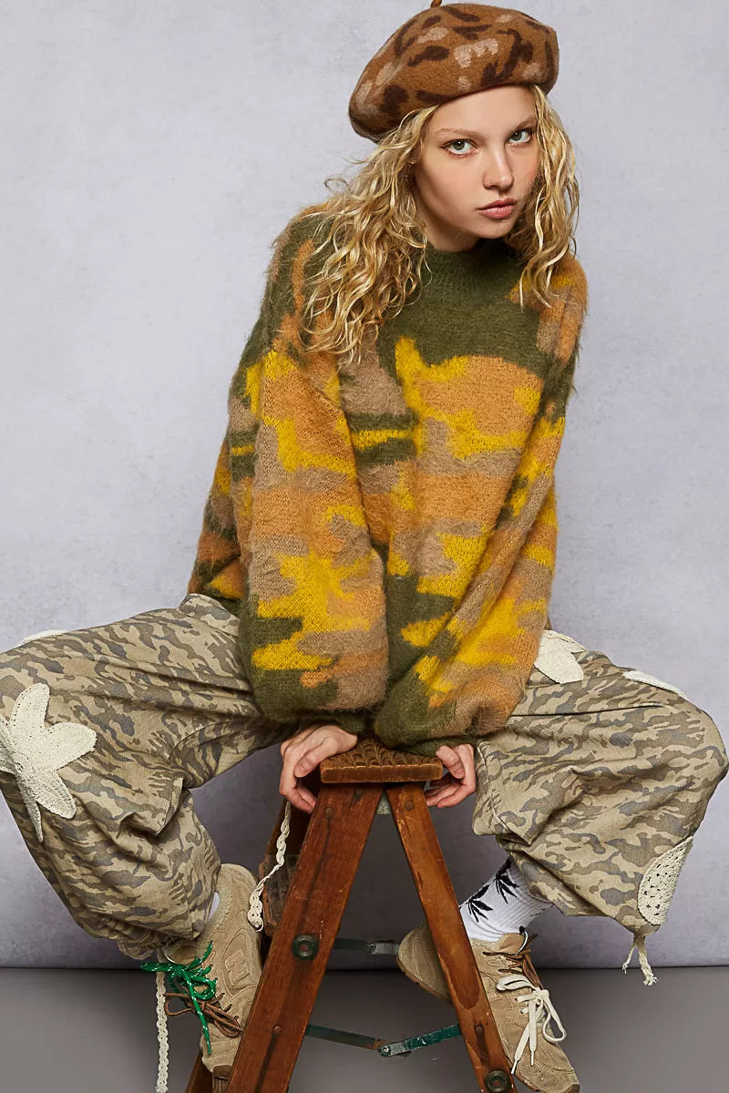 Person wearing a patterned sweater and beret sitting on a stool against a gray background