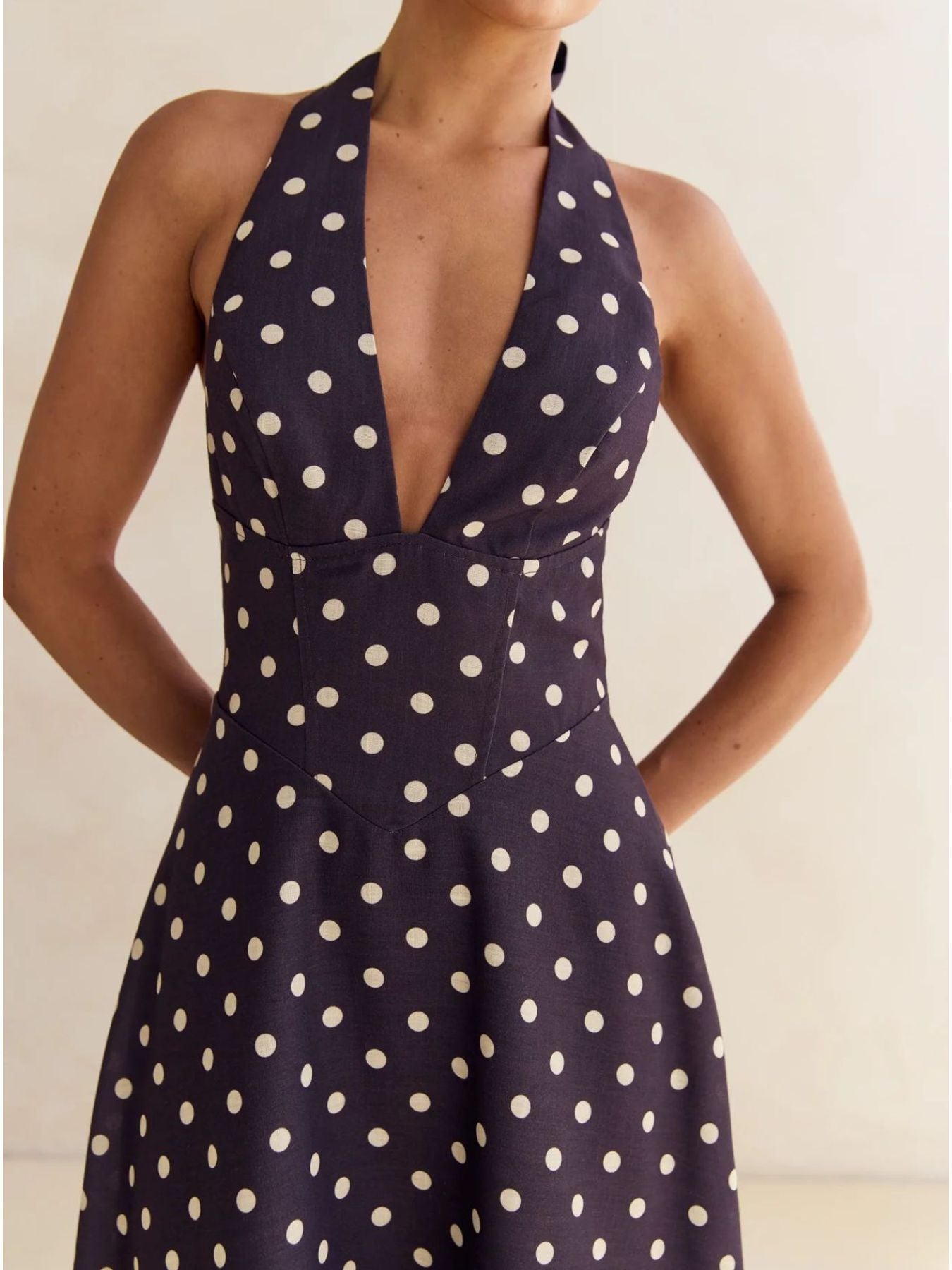 Navy blue dress with white polka dots worn by a model against a neutral background