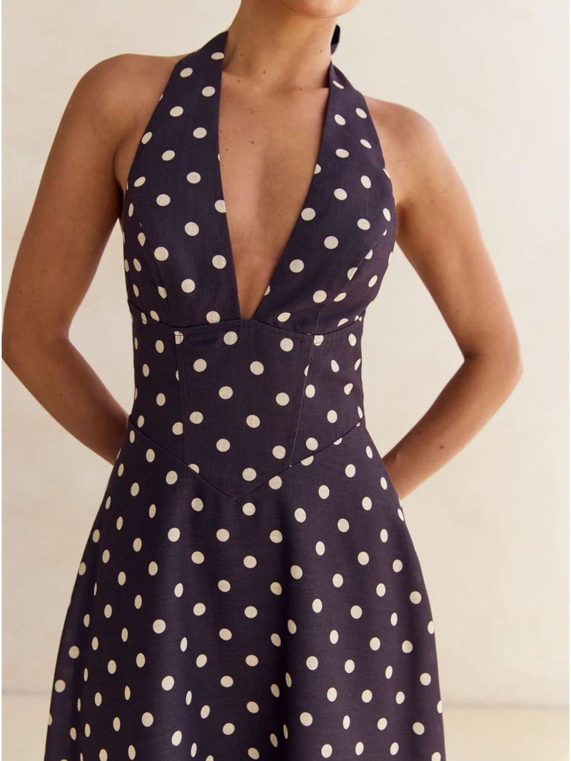 Navy blue dress with white polka dots worn by a model against a neutral background