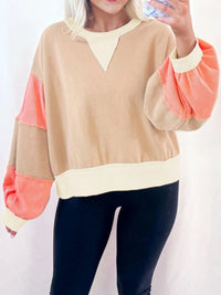 Person wearing a beige and coral sweater with a plain background