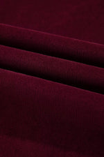 A close-up of draped burgundy knit fabric with soft folds showing its fine ribbed texture.