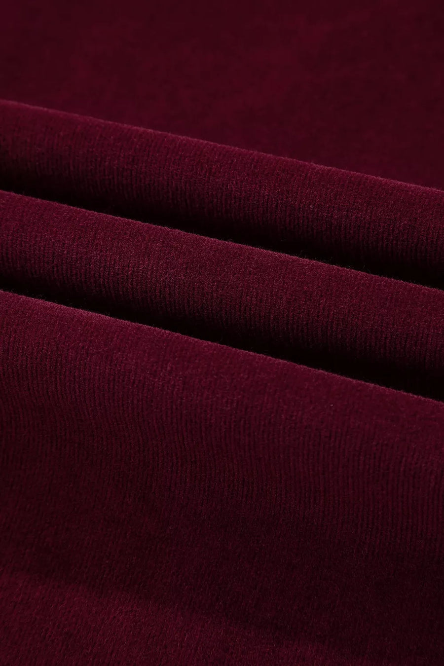 A close-up of draped burgundy knit fabric with soft folds showing its fine ribbed texture.